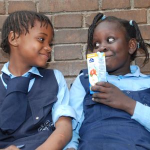 Zwei Schulkinder in Schuluniform sitzen vor einer Ziegelwand