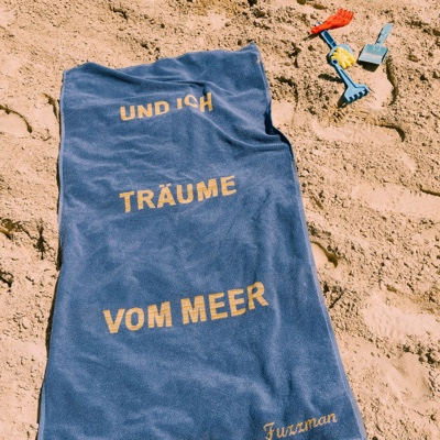 Blaues Badetuch mit Gelber Schrift liegt auf Sandstrand